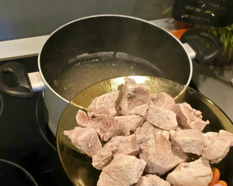 A plate with chunks of cooked pork being prepared to be added to a boiling pot of broth.